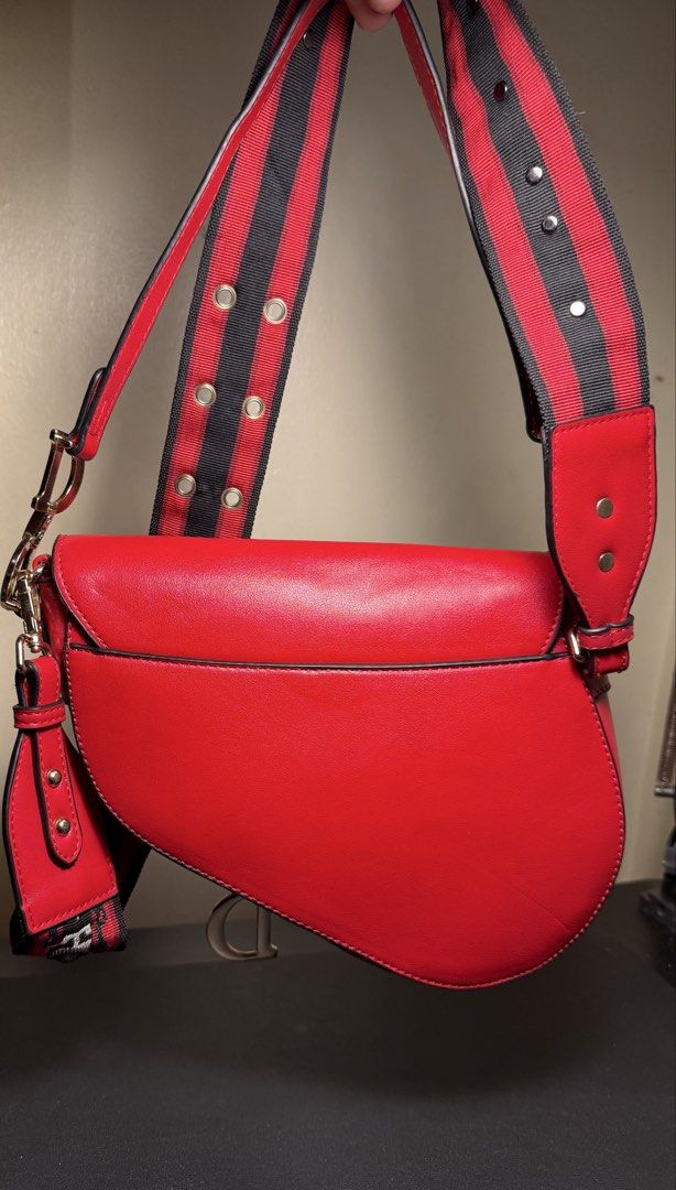 Christian Dior Red Saddle Bag with Embroidered Strap (Category: Luxury Bags & Wallets) located in Manila. Submitted by zuji.ph (Listing ID 1464996788, Image 2). Description: - Brand: Christian Dior Saddle Bag Inspired - Color: Bright Red with gold-tone hardware - Material: Smooth leather finish with iconic hanging 'D' charm - Strap: Thick patterned jacquard shoulder strap in red, black, and white with metal grommet details - Exterior: Convenient 