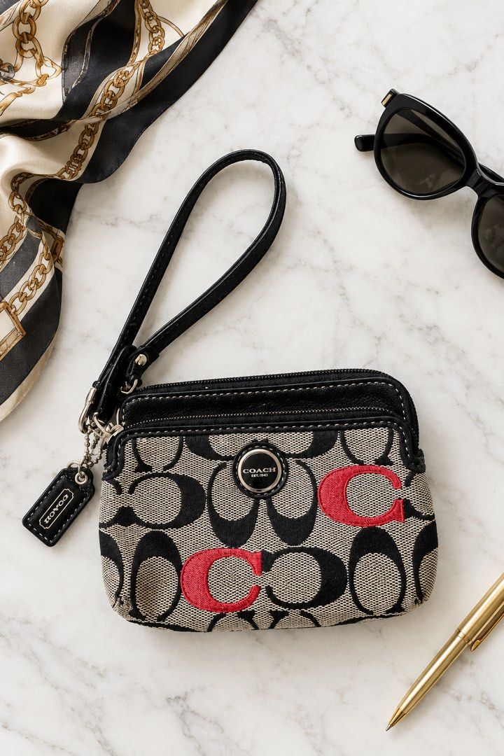 Coach Signature C Double Zip Wristlet (Category: Wallets & Card holders) located in Cebu City. Submitted by relovedfinds.ph (Listing ID 1464994096, Image 1). Description: This authentic Coach wristlet features the classic black signature C pattern with striking red C accents, complemented by a sleek silver-tone front plaque. It comes with a black leather wrist strap and hanging Coach charm, plus a secure double-zip design for keeping cards, keys,