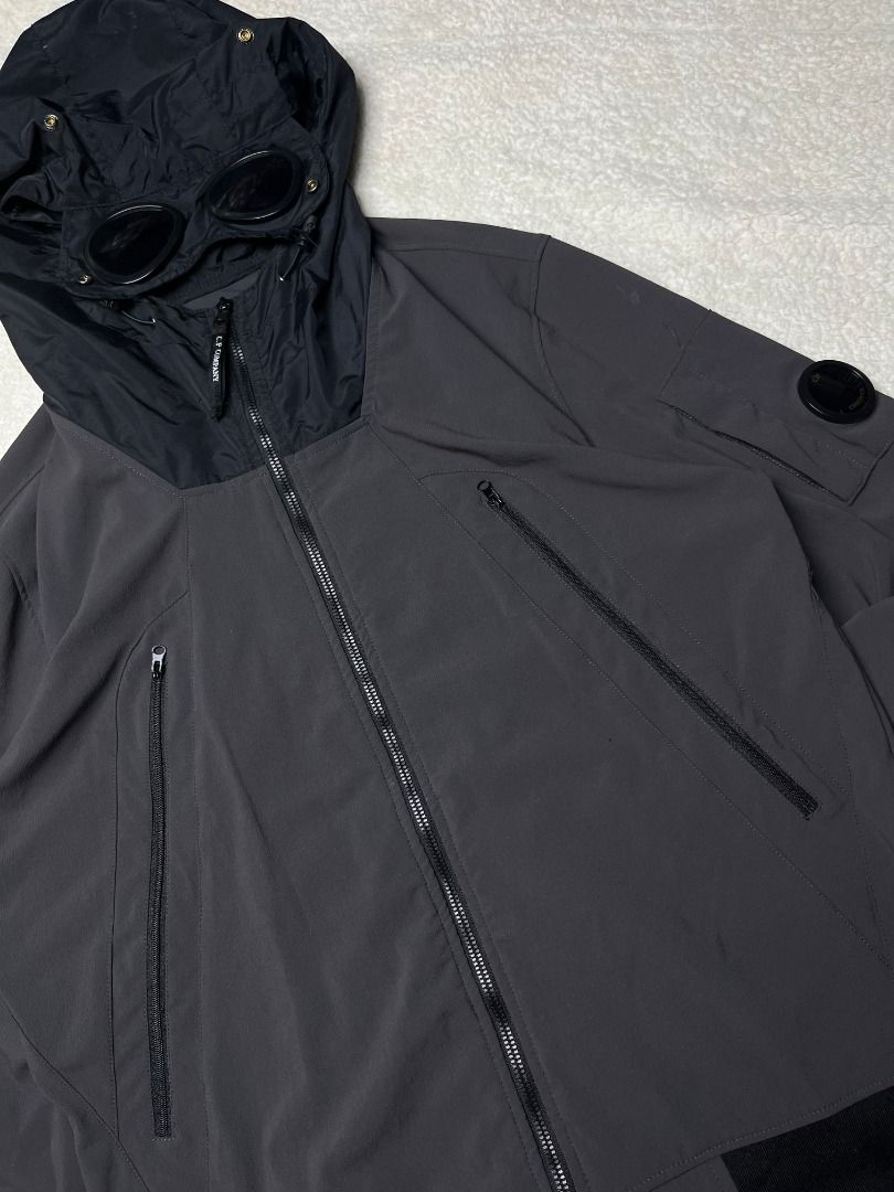 C.P. Company Goggle Hooded Soft Shell Jacket Dark Grey (Category: Coats, Jackets and Outerwear) located in Leyte. Submitted by carlthriftwearapparel (Listing ID 1465008662, Image 1). Description: - Brand: C.P. Company - Color: Dark grey with contrasting black hood - Iconic Details: Built-in goggle lenses on hood and sleeve pocket - Pockets: Multiple zippered pockets on the front - Material: Warm down and white duck feather filling - Features: Rib