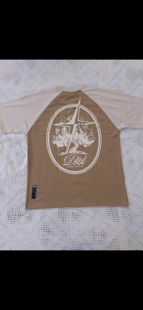 DBTK Raglan T-shirt Brown Beige (Category: Shirts) located in Iloilo. Submitted by franzventures (Listing ID 1464984882, Image 2). Description: - Brand: DBTK - Colorway: Brown and beige raglan - Design: Small cursive embroidery on front chest; large 'Endless Possibilities' tree and star graphic on the back - Details: Short sleeves, round neck, woven label tag near lower hem - Condition: Clean fabric throughout, well-maintained.
