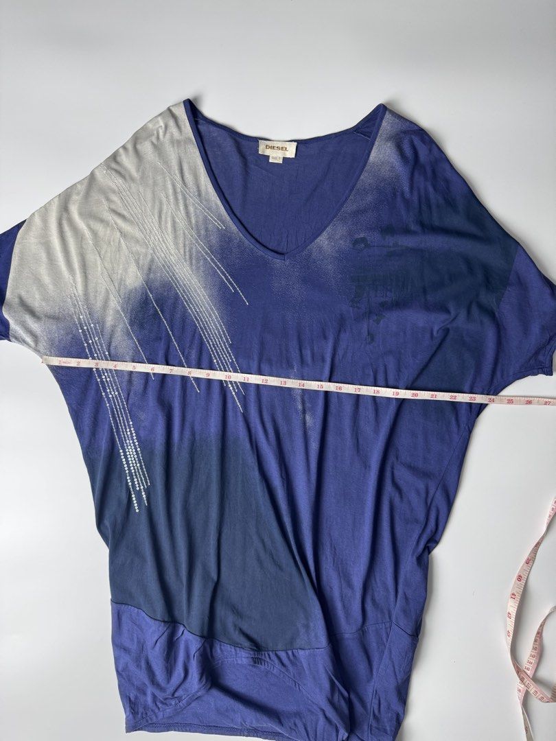 Diesel Blue Gradient V-Neck Top Size S (Category: Blouses) located in Cavite. Submitted by loadeadgears (Listing ID 1465083690, Image 2). Description: - Brand: Diesel - Size: S (tag attached at inner collar) - Color: Blue gradient shades - Style: V-neck top with asymmetrical draped hem - Sleeves: Short dolman sleeves with silver sequin embellishments - Design: Printed graphics on the front chest - Material: Lightweight and comfortable fabric.