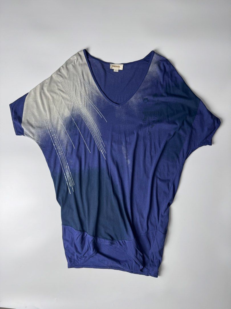 Diesel Blue Gradient V-Neck Top Size S (Category: Blouses) located in Cavite. Submitted by loadeadgears (Listing ID 1465083690, Image 1). Description: - Brand: Diesel - Size: S (tag attached at inner collar) - Color: Blue gradient shades - Style: V-neck top with asymmetrical draped hem - Sleeves: Short dolman sleeves with silver sequin embellishments - Design: Printed graphics on the front chest - Material: Lightweight and comfortable fabric.