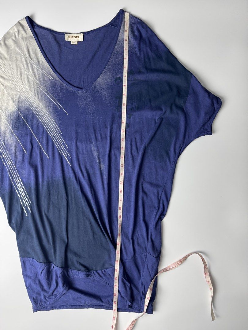 Diesel Blue Gradient V-Neck Top Size S (Category: Blouses) located in Cavite. Submitted by loadeadgears (Listing ID 1465083690, Image 3). Description: - Brand: Diesel - Size: S (tag attached at inner collar) - Color: Blue gradient shades - Style: V-neck top with asymmetrical draped hem - Sleeves: Short dolman sleeves with silver sequin embellishments - Design: Printed graphics on the front chest - Material: Lightweight and comfortable fabric.