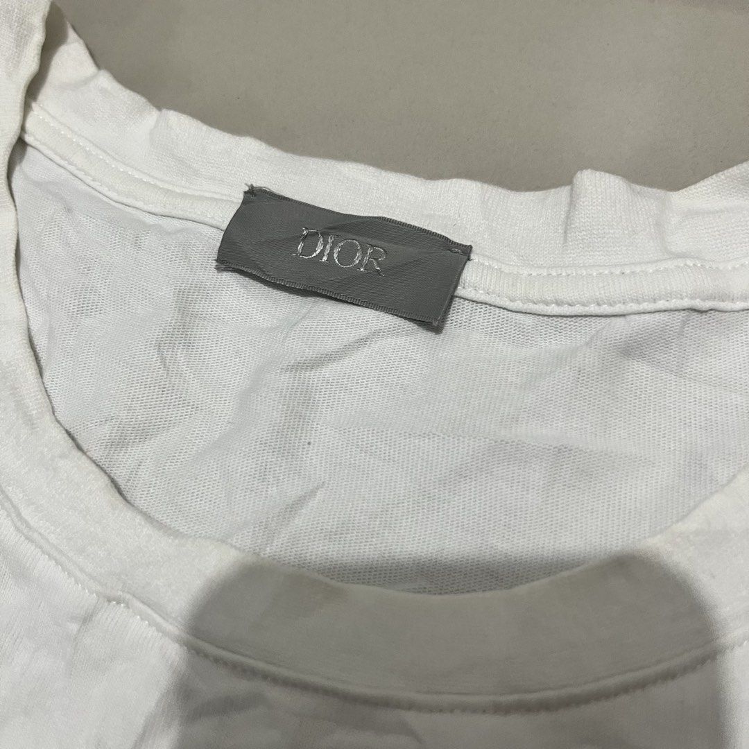 Dior Buffalo Graphic White T-Shirt (Category: Shirts) located in San Fernando. Submitted by cyrelregal27910 (Listing ID 1465124006, Image 3). Description: - Brand: Dior - Size: M (Regular Fit) - Material: 100% cotton with acrylic blend embroidery (Made in Italy) - Design: White tee featuring a blue and white buffalo graphic with intricate typographic details - Style: Crew neck, short sleeves - Condition: Clean tags and wash labels intact.