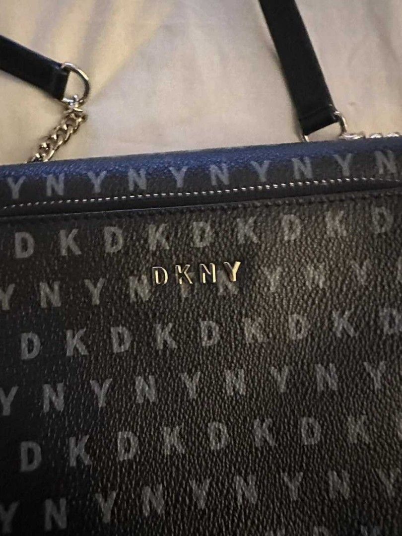 DKNY monogram crossbody bag black (Category: Luxury Bags & Wallets) located in Manila. Submitted by hellocaea010894 (Listing ID 1465115431, Image 2). Description: Black DKNY crossbody bag with all-over DKNY monogram print. Gold hardware lettering on the front pocket. Zip closure with a tassel pull. Long strap with chain detail near the links. Structured rectangular shape with front pocket compartment. Neutral dark tones match casual daily outfits