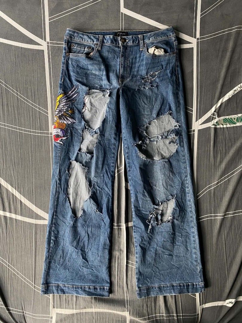 Ed Hardy Distressed Embroidered Denim Jeans (Category: Jeans) located in Manila. Submitted by raymondrob54698 (Listing ID 1465093185, Image 1). Description: - Brand: Ed Hardy - Wash: Mid-blue denim with heavy distressing and rips on both legs - Design: Large embroidered eagle and heart graphic with 'Brave Hearts' and 'Stay True' lettering - Branding: Big white script logo printed across the back waistband and pockets - Fit: Trendy wide leg fit - 