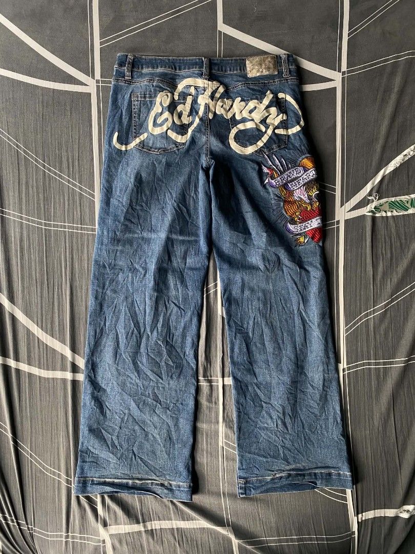 Ed Hardy Distressed Embroidered Denim Jeans (Category: Jeans) located in Manila. Submitted by raymondrob54698 (Listing ID 1465093185, Image 2). Description: - Brand: Ed Hardy - Wash: Mid-blue denim with heavy distressing and rips on both legs - Design: Large embroidered eagle and heart graphic with 'Brave Hearts' and 'Stay True' lettering - Branding: Big white script logo printed across the back waistband and pockets - Fit: Trendy wide leg fit - 