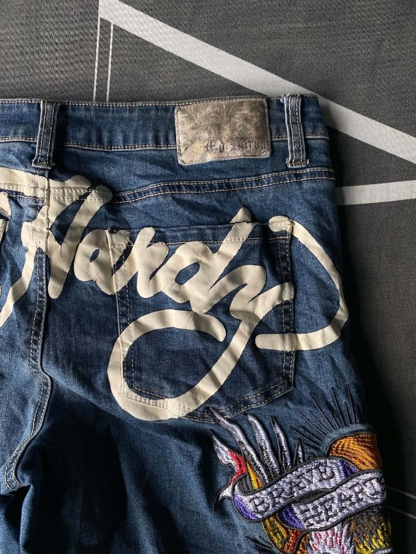 Ed Hardy Distressed Embroidered Denim Jeans (Category: Jeans) located in Manila. Submitted by raymondrob54698 (Listing ID 1465093185, Image 3). Description: - Brand: Ed Hardy - Wash: Mid-blue denim with heavy distressing and rips on both legs - Design: Large embroidered eagle and heart graphic with 'Brave Hearts' and 'Stay True' lettering - Branding: Big white script logo printed across the back waistband and pockets - Fit: Trendy wide leg fit - 
