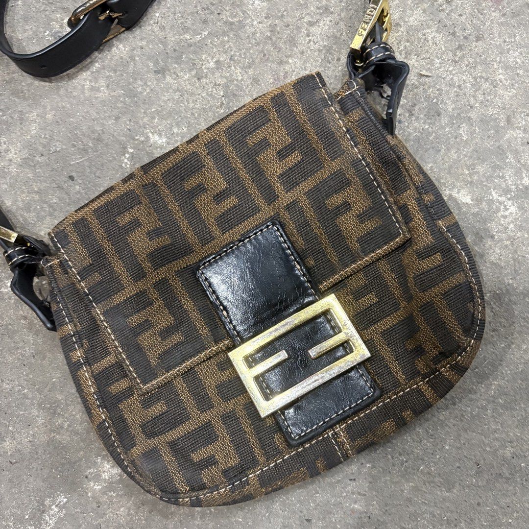 Fendi Mini Zucca FF Baguette (Category: Luxury Bags & Wallets) located in Zamboanga. Submitted by thriftyyali (Listing ID 1465100795, Image 2). Description: - Authentic Fendi Zucca canvas pattern in classic brown and black - Sleek black leather strap and front magnetic flap closure - Elegant gold-tone hardware with engraved FENDI lettering - Stamped 'Made in Italy' tag near the front lock mechanism - Perfect luxury everyday or statement bag.