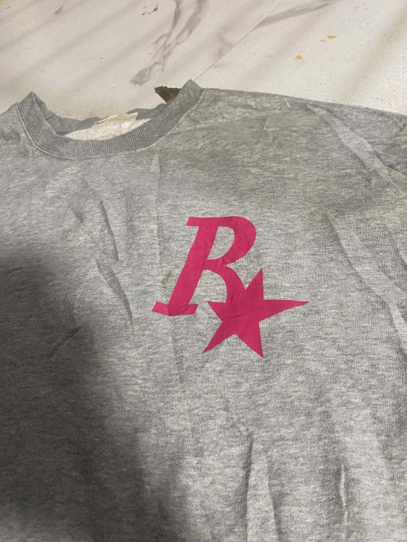 Grey Rockstar Games Logo Sweatshirt (Category: Coats, Jackets and Outerwear) located in Abucay. Submitted by vonnmercad90612 (Listing ID 1465154855, Image 1). Description: - Brand/Design: Grey oversized sweatshirt with bright pink Rockstar Games 'R' logo on both chest and back - Fit & Feel: Comfortable oversized fit with ribbed collar, cuffs, and hem; fabric feels soft and broken-in - Condition: Minor wear visible near the front logo area - Ideal
