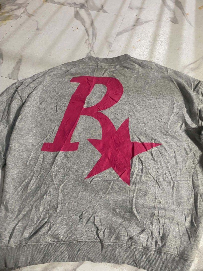 Grey Rockstar Games Logo Sweatshirt (Category: Coats, Jackets and Outerwear) located in Abucay. Submitted by vonnmercad90612 (Listing ID 1465154855, Image 2). Description: - Brand/Design: Grey oversized sweatshirt with bright pink Rockstar Games 'R' logo on both chest and back - Fit & Feel: Comfortable oversized fit with ribbed collar, cuffs, and hem; fabric feels soft and broken-in - Condition: Minor wear visible near the front logo area - Ideal