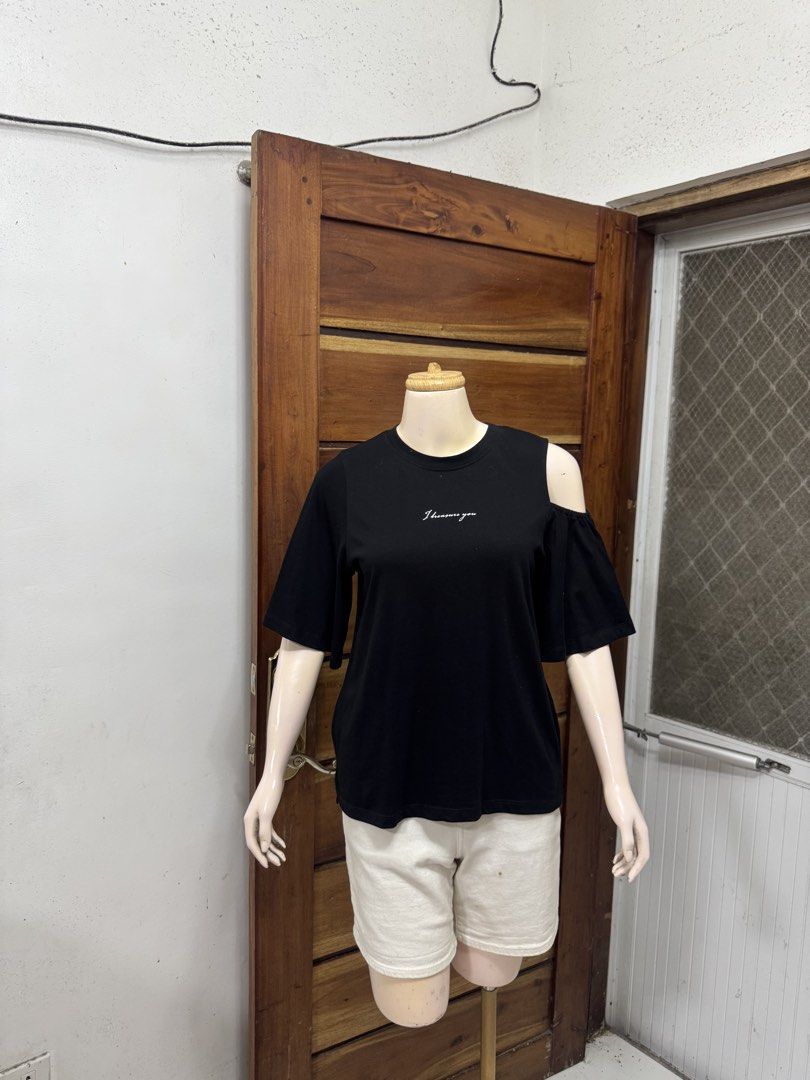 GU (Category: Shirts) located in Cavite. Submitted by yakultjeni85475 (Listing ID 1465123923, Image 3). Description: - Color: Black - Material: Soft, comfortable cotton - Fit: Relaxed fit with short sleeves - Design: Asymmetrical cold-shoulder cutout on the left - Detail: 'I treasure you' white script lettering on the chest - Style: Easy to pair with shorts or denim for everyday casual fits.