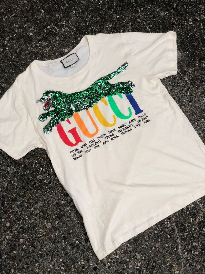 Gucci Sequin Tiger Multicolor Cities Logo T-Shirt (Category: Luxury Apparel) located in Tacloban City. Submitted by thedropout (Listing ID 1465050935, Image 1). Description: - Authentic Gucci graphic tee in off-white cotton - Features vibrant multicolor rainbow lettering with city names - Stunning green sequin tiger patch meticulously stitched on the front - Premium heavyweight fabric with a pristine, clean collar - Includes classic Gucci interio