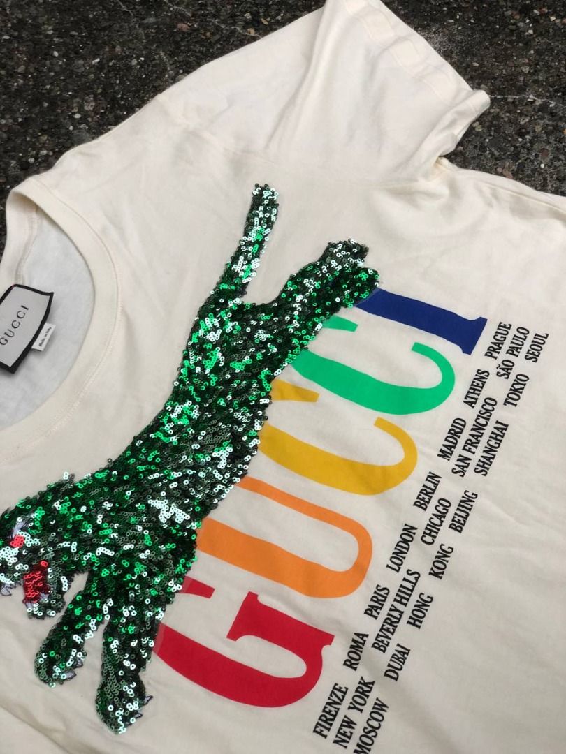 Gucci Sequin Tiger Multicolor Cities Logo T-Shirt (Category: Luxury Apparel) located in Tacloban City. Submitted by thedropout (Listing ID 1465050935, Image 3). Description: - Authentic Gucci graphic tee in off-white cotton - Features vibrant multicolor rainbow lettering with city names - Stunning green sequin tiger patch meticulously stitched on the front - Premium heavyweight fabric with a pristine, clean collar - Includes classic Gucci interio