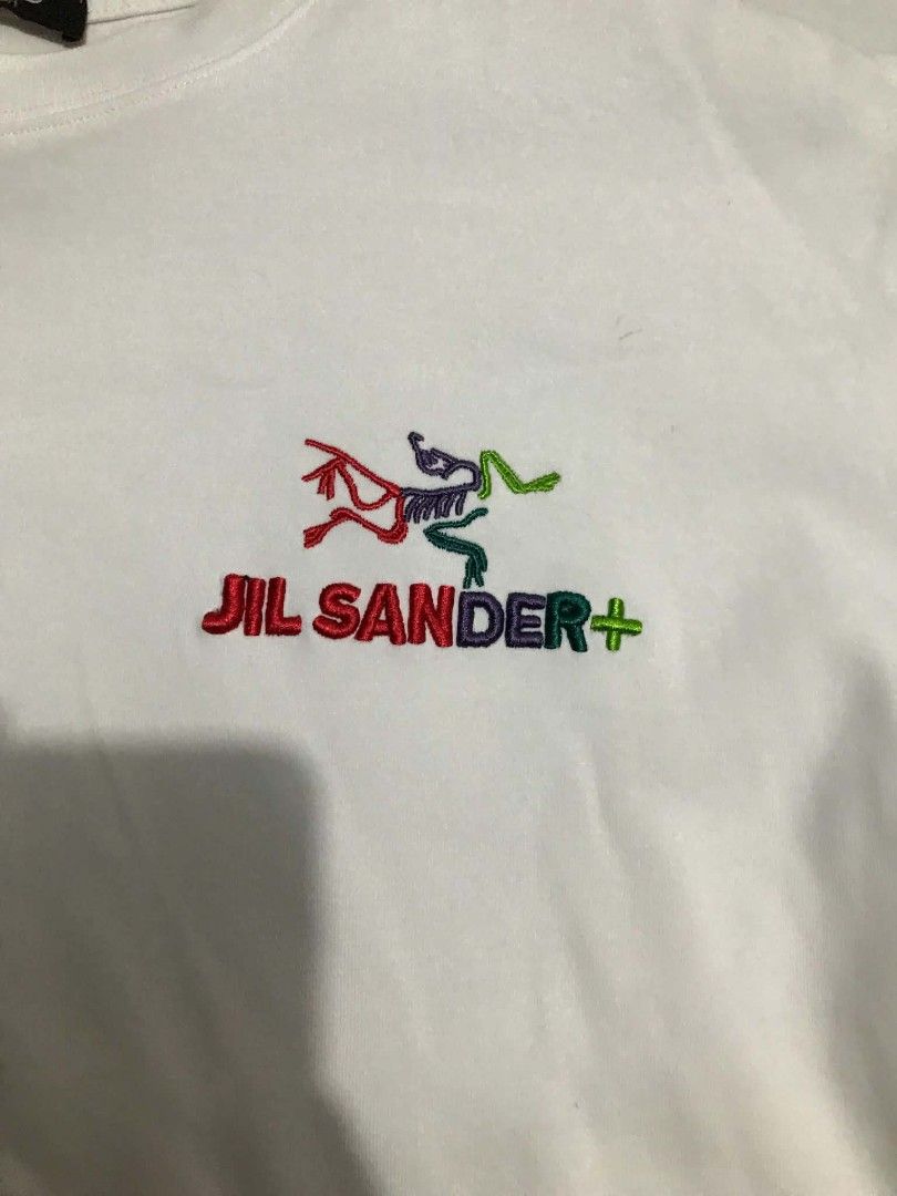 Jil Sander x Arc'teryx White Graphic Tee (Category: Shirts) located in Manila. Submitted by mikeee03 (Listing ID 1465137773, Image 2). Description: - Brand: Jil Sander x Arc'teryx - Color: White - Style: Short sleeve crewneck t-shirt - Details: Embroidered multi-colored chest logo with Jil Sander+ text - Back Design: Large green and dark blue square graphic with Arc'teryx skeletal design - Condition: Good asnew - Sobrang kapal ng tela Need wash o