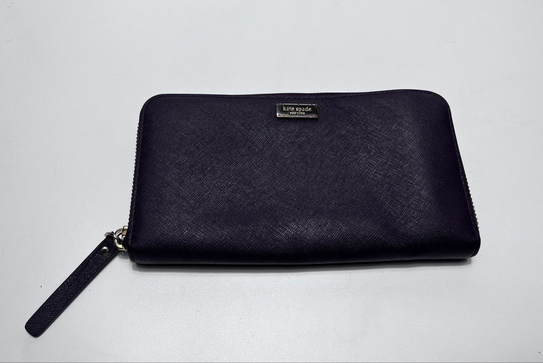 Kate Spade New York Zip Around Wallet (Category: Wallets & Card holders) located in Iloilo. Submitted by fromthebins.ilo2 (Listing ID 1465000473, Image 1). Description: - Brand: Kate Spade New York - Color: Deep purple - Material: Genuine leather with signature pink patterned fabric lining - Closure: Zip-around with a matching wrist strap - Interior Features: Multiple card slots, slip compartments, and a zippered coin pocket - Exterior: Gold meta