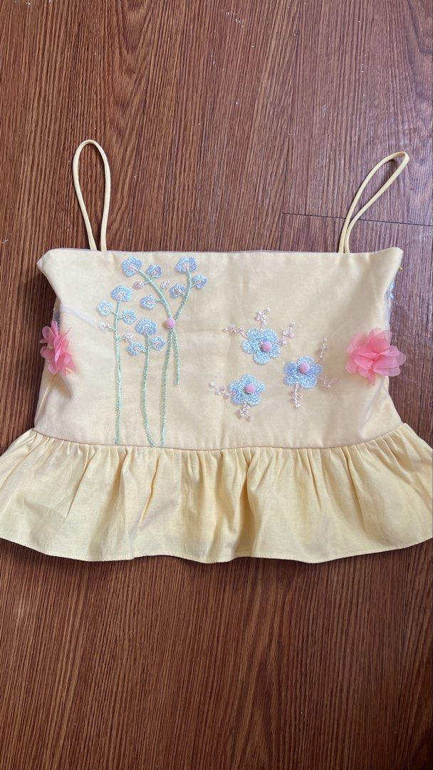 La Coco Babe Top (XS) (Category: Sleeveless) located in Manila. Submitted by d.rosie844 (Listing ID 1465081945, Image 1). Description: - Brand: La Coco Babe - Size: XS (EU 34 / UK 6 / US 2) - Color: Pastel Yellow - Design: Delicate blue floral embroidery with cute 3D pink flower appliqués on the sides and a ruffled hem - Condition: Layered condition 4, well-maintained - Meetup Location: Scout Borromeo, Quezon City.