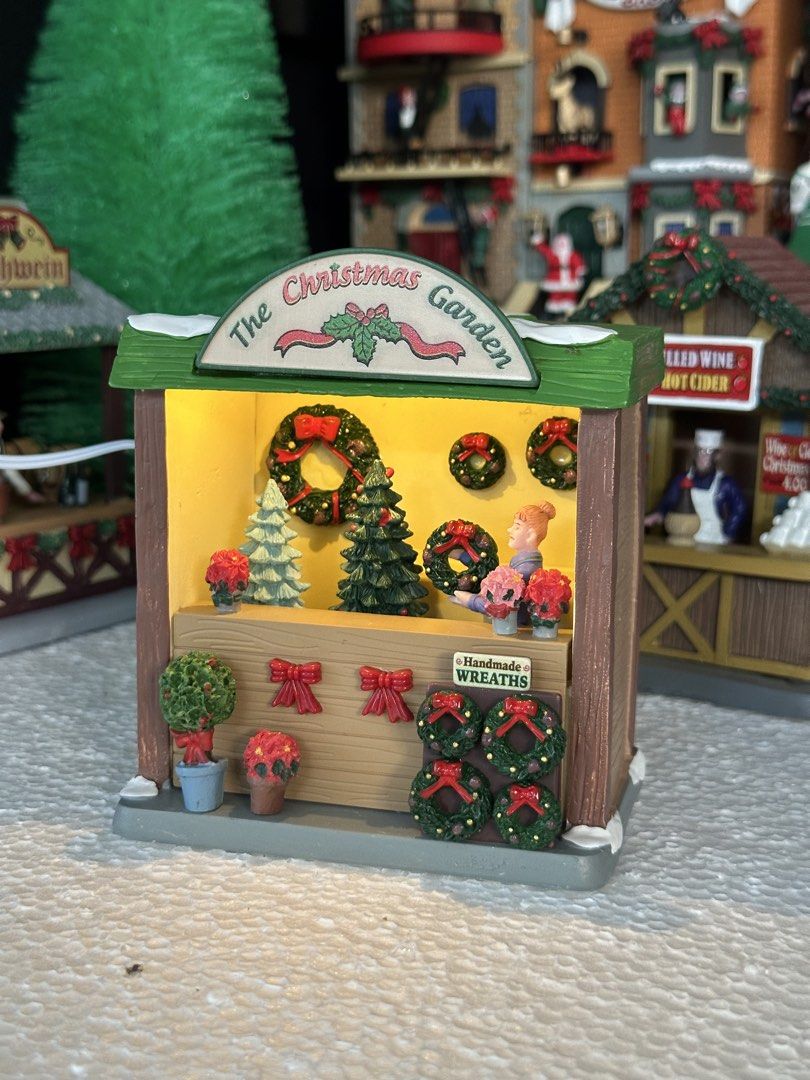 Lemax The Christmas Garden (Category: Figurines & Statues) located in Santiago. Submitted by kitalpanga (Listing ID 1465062838, Image 2). Description: Lighted. Adaptor not included - Miniature holiday market stall named 'The Christmas Garden' - Includes a shopkeeper figure holding a green wreath behind the counter - Features detailed handmade wreaths, small potted poinsettias, and decorated evergreen trees - Designed with a festive green roof and