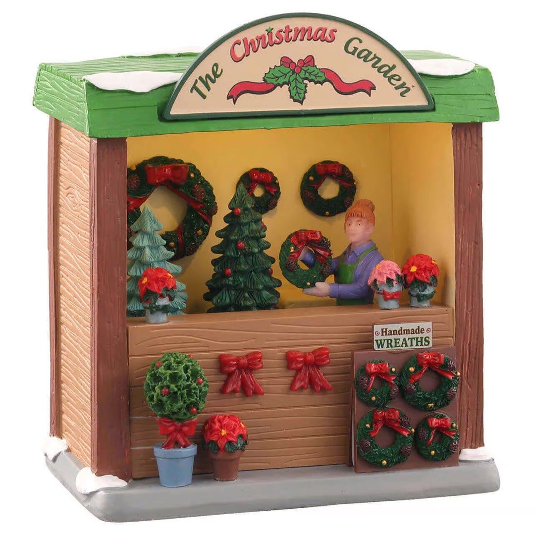 Lemax The Christmas Garden (Category: Figurines & Statues) located in Santiago. Submitted by kitalpanga (Listing ID 1465062838, Image 1). Description: Lighted. Adaptor not included - Miniature holiday market stall named 'The Christmas Garden' - Includes a shopkeeper figure holding a green wreath behind the counter - Features detailed handmade wreaths, small potted poinsettias, and decorated evergreen trees - Designed with a festive green roof and