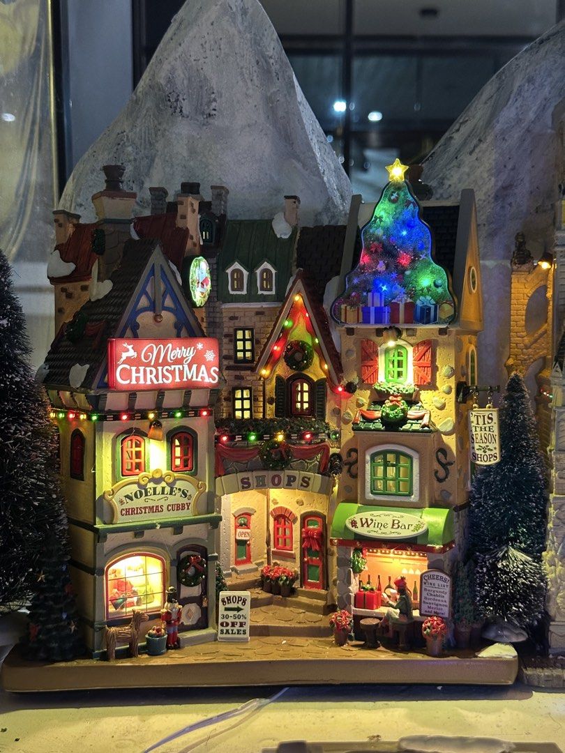 Lemax Tis The Season Shops Facade (Category: Figurines & Statues) located in Santiago. Submitted by kitalpanga (Listing ID 1465066054, Image 2). Description: Battery operated / 4.5v adaptable - Festive multi-story Christmas village design - Features colorful shops, a wine bar, nutcracker, wreaths, and holiday signs - Lights up with a large glowing tree and warm window lights - Crafted from durable, heavy resin - Perfect holiday centerpiece for ma