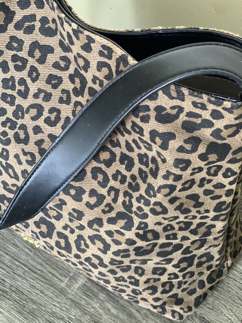 Leopard Print Canvas Shoulder Tote Bag (Category: Shoulder Bags) located in Pili. Submitted by gaellecast (Listing ID 1464968966, Image 2). Description: - Style: Leopard print shoulder bag / everyday tote - Material: Canvas body with black faux leather handles - Hardware: Gold buckle adjustments and front logo stamp - Interior: Light-colored lining with 1 zip pocket and 1 open slot.