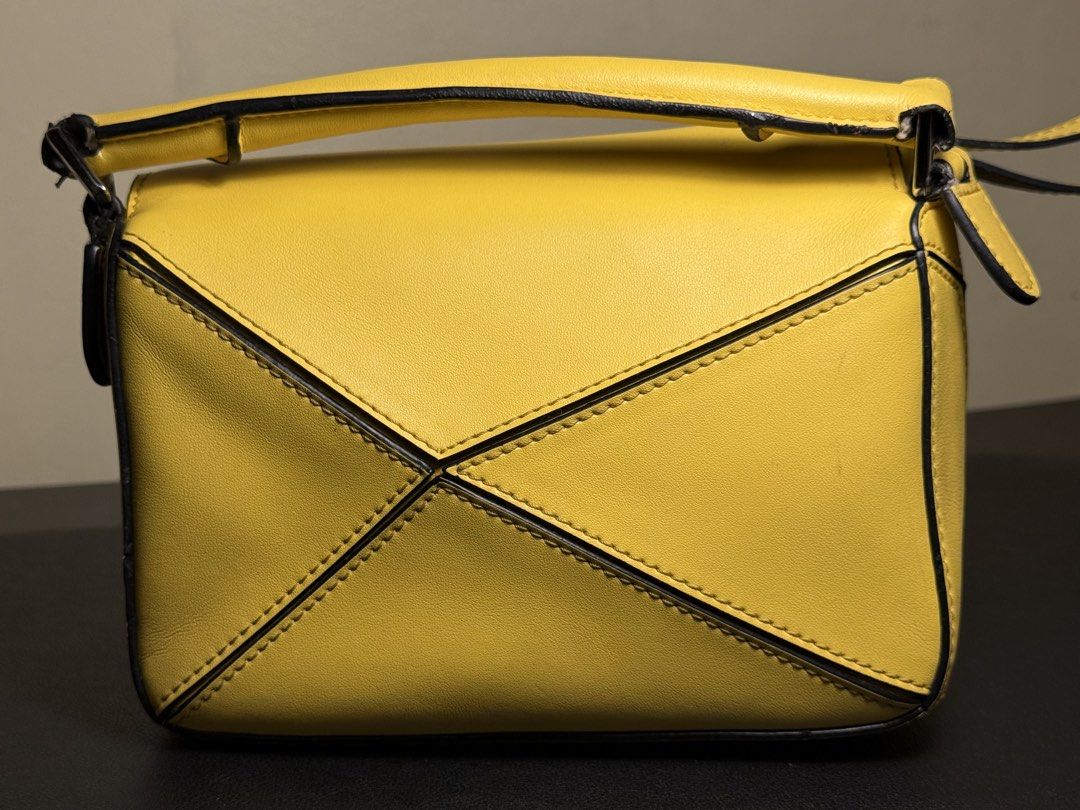 Loewe Puzzle Bag Yellow (Category: Luxury Bags & Wallets) located in Manila. Submitted by zuji.ph (Listing ID 1464998424, Image 1). Description: Bright yellow leather Loewe Puzzle bag. Distinct geometric panel design with black edge painting. Top handle configuration and structured shape. Interior lined with herringbone fabric, branded leather tag, and white origin label stamped Made in Spain. Compact shoulder or handheld style..