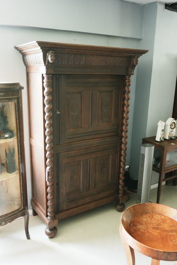 Louis XIII-Style Carved Cupboard (Category: Shelves, Cabinets & Racks) located in Manila. Submitted by heleensym (Listing ID 1464970833, Image 1). Description: An architectural wooden cupboard framed by full-height barley-twist columns and topped with a richly carved cornice featuring two expressive faces. Floral panel carving, patterned borders, and rounded bun feet complete the design. Separate upper and lower doors open to shelved storage, mak