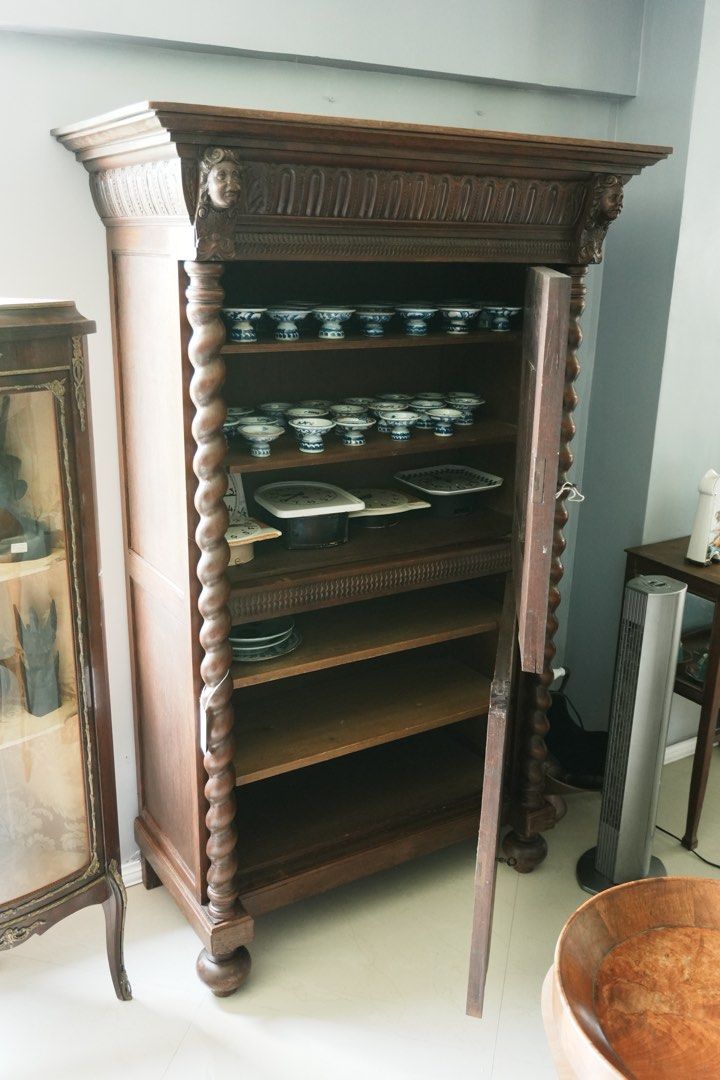 Louis XIII-Style Carved Cupboard (Category: Shelves, Cabinets & Racks) located in Manila. Submitted by heleensym (Listing ID 1464970833, Image 2). Description: An architectural wooden cupboard framed by full-height barley-twist columns and topped with a richly carved cornice featuring two expressive faces. Floral panel carving, patterned borders, and rounded bun feet complete the design. Separate upper and lower doors open to shelved storage, mak