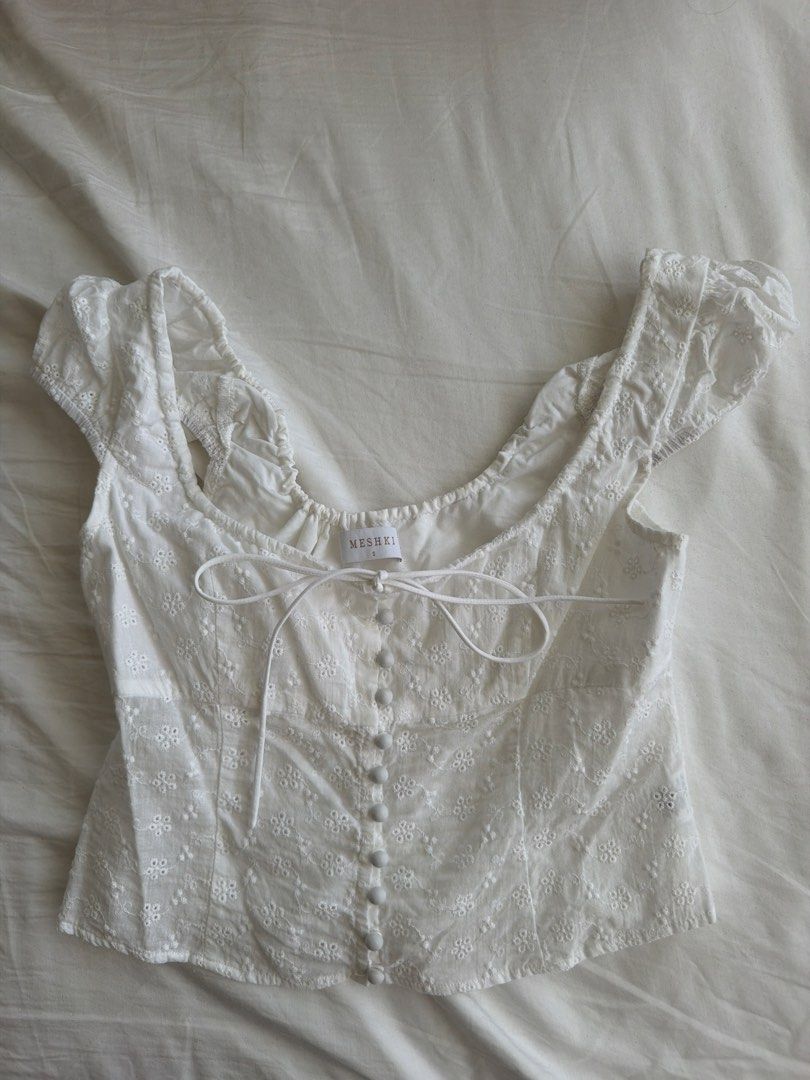 MESHKI White Embroidered Lace Crop Top (Category: Sleeveless) located in Cavite. Submitted by klarev (Listing ID 1465010600, Image 1). Description: - Color: White - Size: Small - Material: Lightweight fabric with all-over eyelet embroidery - Design: Scoop neckline with string tie, front button-down closure, and short cap sleeves with ruffled hem.