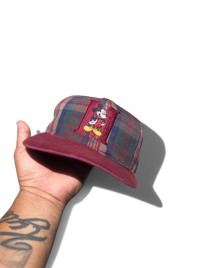 Mickey Unlimited Plaid Snapback Hat Disney (Category: Caps & Hats) located in Dasmarinas. Submitted by insaurigaj60770 (Listing ID 1465133429, Image 1). Description: - Brand: Mickey Unlimited (Made in China) - Design: Classic plaid pattern with burgundy flat brim and maroon snapback closure - Front Detail: Embroidered Mickey Mouse graphic over a large letter H applique - Back Detail: Stitched 'Mickey Mouse' script above the strap - Condition: Vin