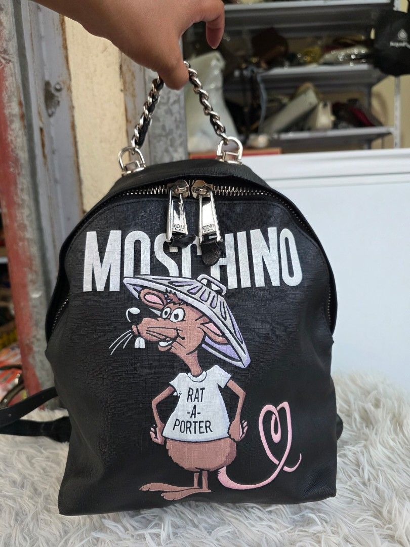 Moschino Rat-A-Porter Backpack Black (Category: Backpacks) located in Lemery. Submitted by venus23 (Listing ID 1465095508, Image 1). Description: - Brand: Moschino - Style: Rat-A-Porter Backpack - Color: Black with striking white branding & cartoon rat print - Material: Durable Saffiano-style textured finish - Hardware: Silver-tone Moschino Milano stamped zips with chain handle detail - Size: Practical everyday size, approx. 11 inches across - Co