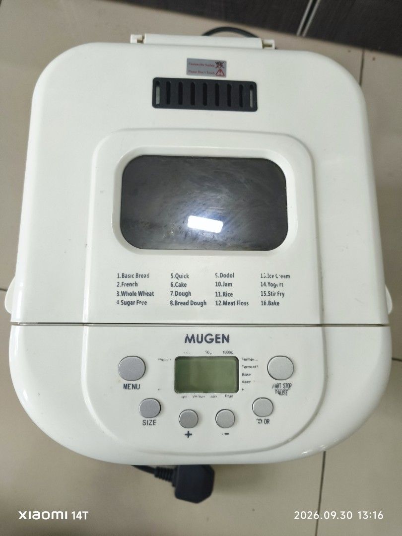 Mugen Automatic Bread Maker Machine (Category: Breadmakers) located in Shah Alam. Submitted by zaharein (Listing ID 1465008449, Image 2). Description: - Brand: Mugen XBM-6000 1kg Automatic Bread Maker - Design: Stainless steel body with a white top lid and digital control panel - Versatile Functions: Multiple menu options including basic bread, cake, dough, jam, and yogurt - Included Accessories: Non-stick baking pan and kneading paddle - Power: 