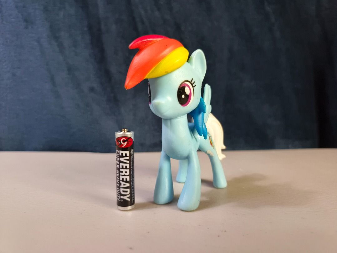 My Little Pony Rainbow Dash Figure (Category: Figurines & Statues) located in San Leonardo. Submitted by burgossanleonardo.12345 (Listing ID 1465052749, Image 2). Description: - Character: Rainbow Dash from My Little Pony - Appearance: Light blue body with a rainbow mane and white tail - Size: Approximately the height of an AA battery - Condition: Minor scuffs and marks from play, but stands completely on its own - Perfect for collectors, kids, o