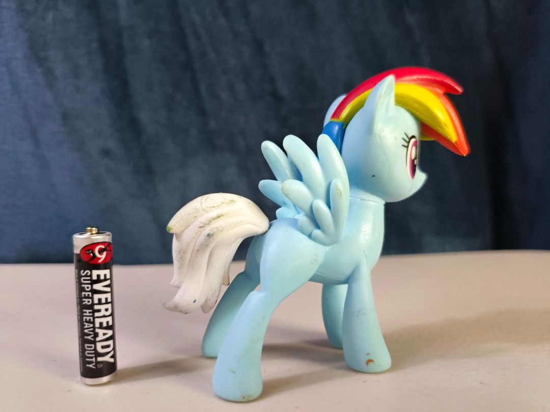 My Little Pony Rainbow Dash Figure (Category: Figurines & Statues) located in San Leonardo. Submitted by burgossanleonardo.12345 (Listing ID 1465052749, Image 3). Description: - Character: Rainbow Dash from My Little Pony - Appearance: Light blue body with a rainbow mane and white tail - Size: Approximately the height of an AA battery - Condition: Minor scuffs and marks from play, but stands completely on its own - Perfect for collectors, kids, o
