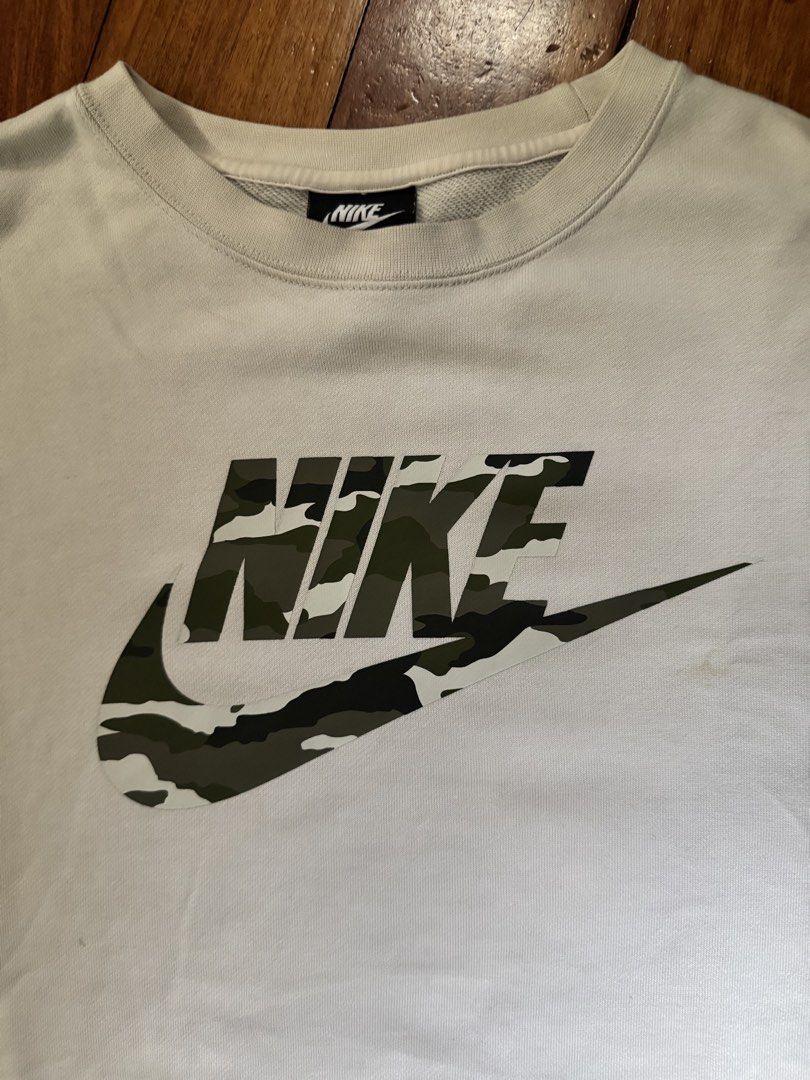 Nike Camo Logo White Sweatshirt (Category: Hoodies) located in Caloocan City. Submitted by gabbieerfritter (Listing ID 1465143177, Image 2). Description: - Brand: Nike - Style: Crewneck sweatshirt - Color: White with big camo graphic logo on the chest - Size: XL - Material: 80% cotton, 20% polyester blend (Made in China) - Condition: Normal wear with slight discoloration near the logo, still warm and comfortable.