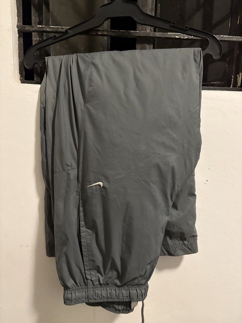 Nike Grey Nylon Track Pants Size L (Category: Joggers) located in Pakil. Submitted by lucii_4 (Listing ID 1465163431, Image 1). Description: - Brand: Nike - Item: Track Pants - Color: Grey - Size: Large (L) - Material: 100% nylon outer with polyester lining - Fit: Elastic waistband with adjustable drawstring - Pockets: Convenient zipper pocket on the back right side - Details: Small white Nike swoosh logo on front left thigh - Origin: Made in Vie