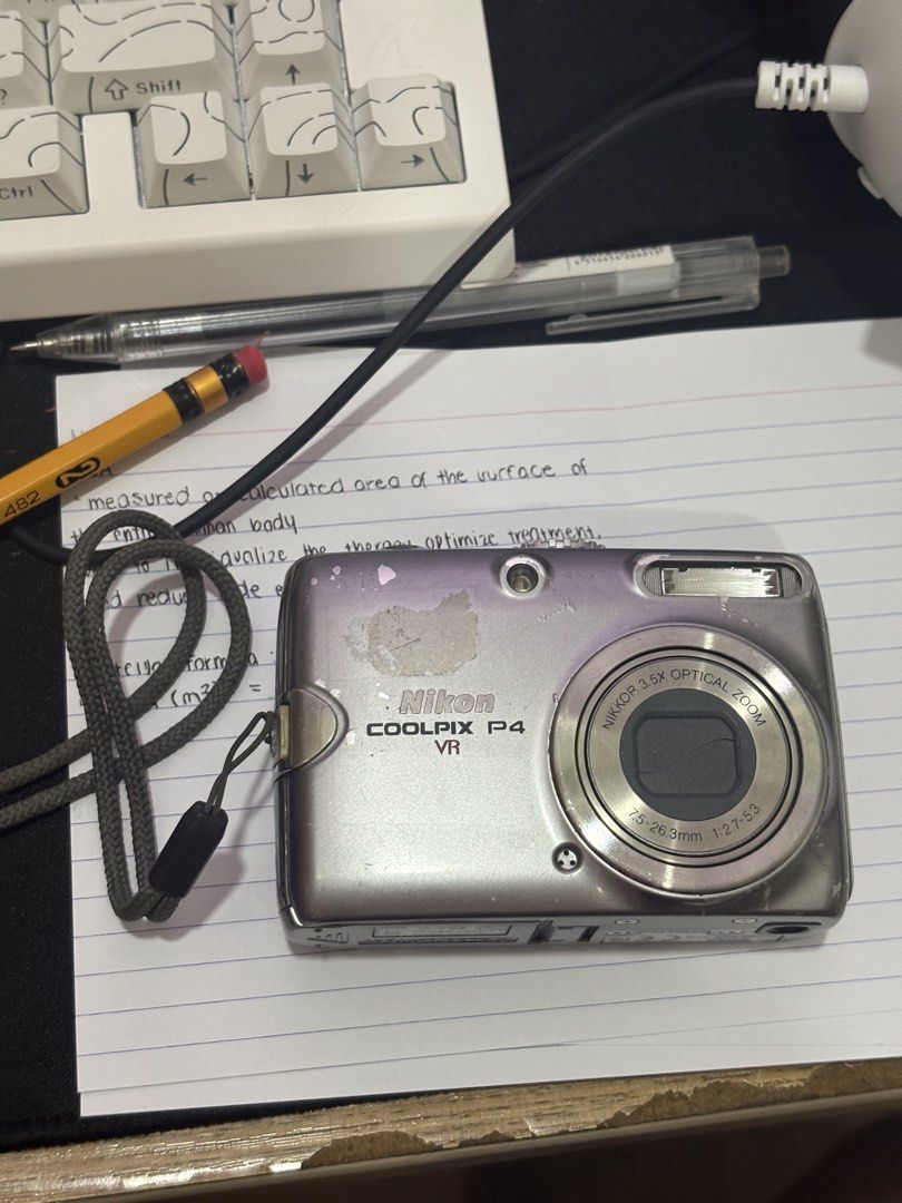 Nikon Coolpix P4 VR (Category: Cameras) located in Manila. Submitted by wohainie (Listing ID 1465070090, Image 1). Description: - Camera Model: Nikon Coolpix P4 VR point and shoot digital camera (Silver) - Lens: Built-in nikon 3.5x optical zoom lens - Condition: Heavy cosmetic wear, scuffs, paint chipping, and heavy marks on the LCD screen - Functionality: Powers on/off via top buttons and dial, tested working - Inclusions: Wrist strap attached -