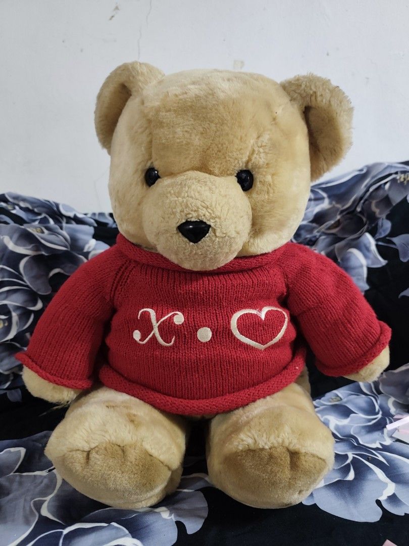 Plush Teddy Bear in Red Sweater with Heart (Category: Plushies & Soft Toys) located in Manila. Submitted by gelvy1316 (Listing ID 1465056121, Image 2). Description: - Product: Fluffy teddy bear with soft light brown fur and dark button eyes - Outfit: Cozy red knitted sweater with embroidered white "X.O." and heart lettering - Condition: Brand new, still in original plastic packaging adorned with a pink ribbon - Ideal Use: Perfect as a thoughtful 