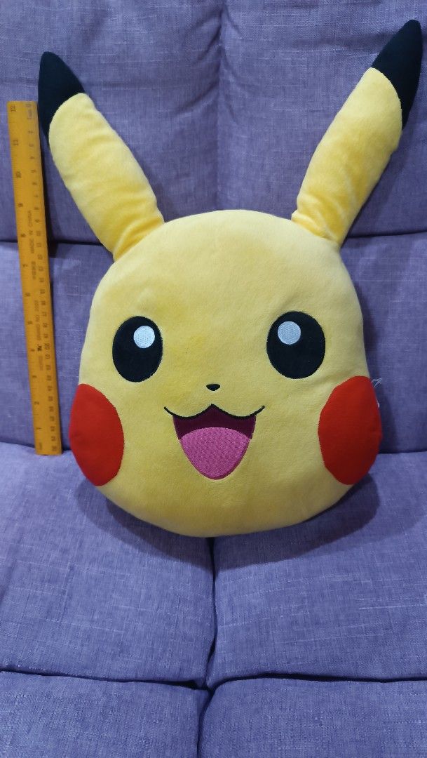 Pokémon Pikachu Head Plush Pillow (Category: Plushies & Soft Toys) located in Quezon City. Submitted by fabricatebycp (Listing ID 1465112774, Image 2). Description: Pikachu head plush pillow, bright yellow with red cheeks and embroidered smiling face. Measures roughly thirty centimeters across based on the ruler measurement shown. Tag says The ONE, includes copyright text dated 1997 Nintendo and Pokémon on the reverse side. Soft fabric material, 