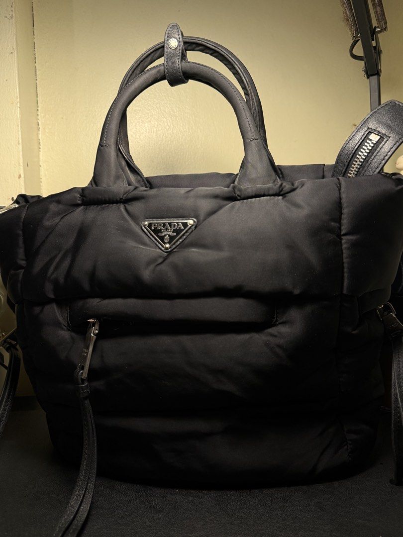 Prada Black Nylon Puffer Handbag Tote (Category: Luxury Bags & Wallets) located in Manila. Submitted by zuji.ph (Listing ID 1464995783, Image 1). Description: -black Prada puffer nylon tote bag - Iconic front triangle logo plaque and sleek silver-tone hardware - Practical double top handles and secure top zip closure with Lampo zipper pull - Convenient zippered outer pocket on the front body - Fully lined black fabric interior with Prada Milano m