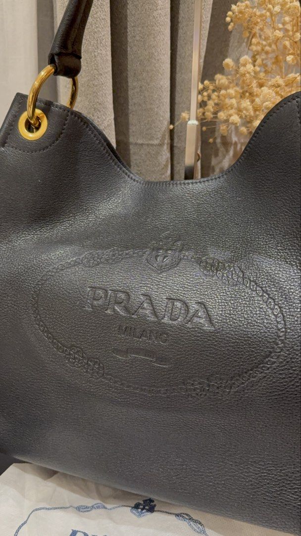 Prada Vitello Daino Embossed Logo Hobo (Category: Luxury Bags & Wallets) located in Quezon City. Submitted by mamadeclutter8877 (Listing ID 1465092809, Image 2). Description: - Authentic Prada shoulder bag in black grained leather - Features a large embossed logo on the front and classic enamel triangle logo on the side - Elegant gold-tone hardware rings - Comfortable single rounded leather handle - Slouchy, spacious interior perfect for daily es