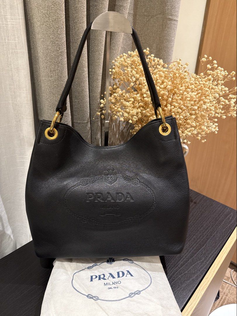 Prada Vitello Daino Embossed Logo Hobo (Category: Luxury Bags & Wallets) located in Quezon City. Submitted by mamadeclutter8877 (Listing ID 1465092809, Image 1). Description: - Authentic Prada shoulder bag in black grained leather - Features a large embossed logo on the front and classic enamel triangle logo on the side - Elegant gold-tone hardware rings - Comfortable single rounded leather handle - Slouchy, spacious interior perfect for daily es