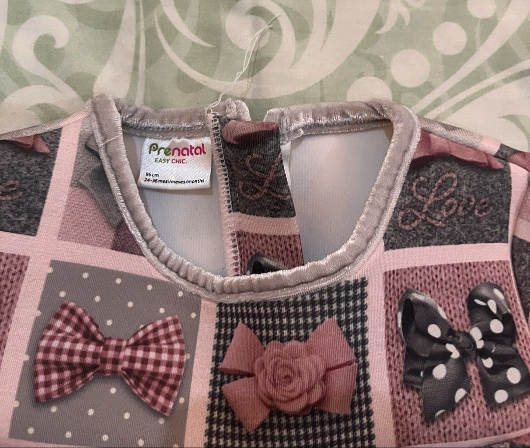 Prénatal Easy Chic Bow Pattern Toddler Dress Size 96cm (Category: Babies & Kids Fashion) located in Batangas. Submitted by gavsandrix (Listing ID 1465048667, Image 3). Description: - Brand: Prénatal Easy Chic - Size: 96cm (fits ages 24 to 36 months) - Design: Soft pink background with grey, black, and red square pattern blocks featuring various bow designs - Features: Short sleeves, flared skirt silhouette, and a convenient small loop closure at 