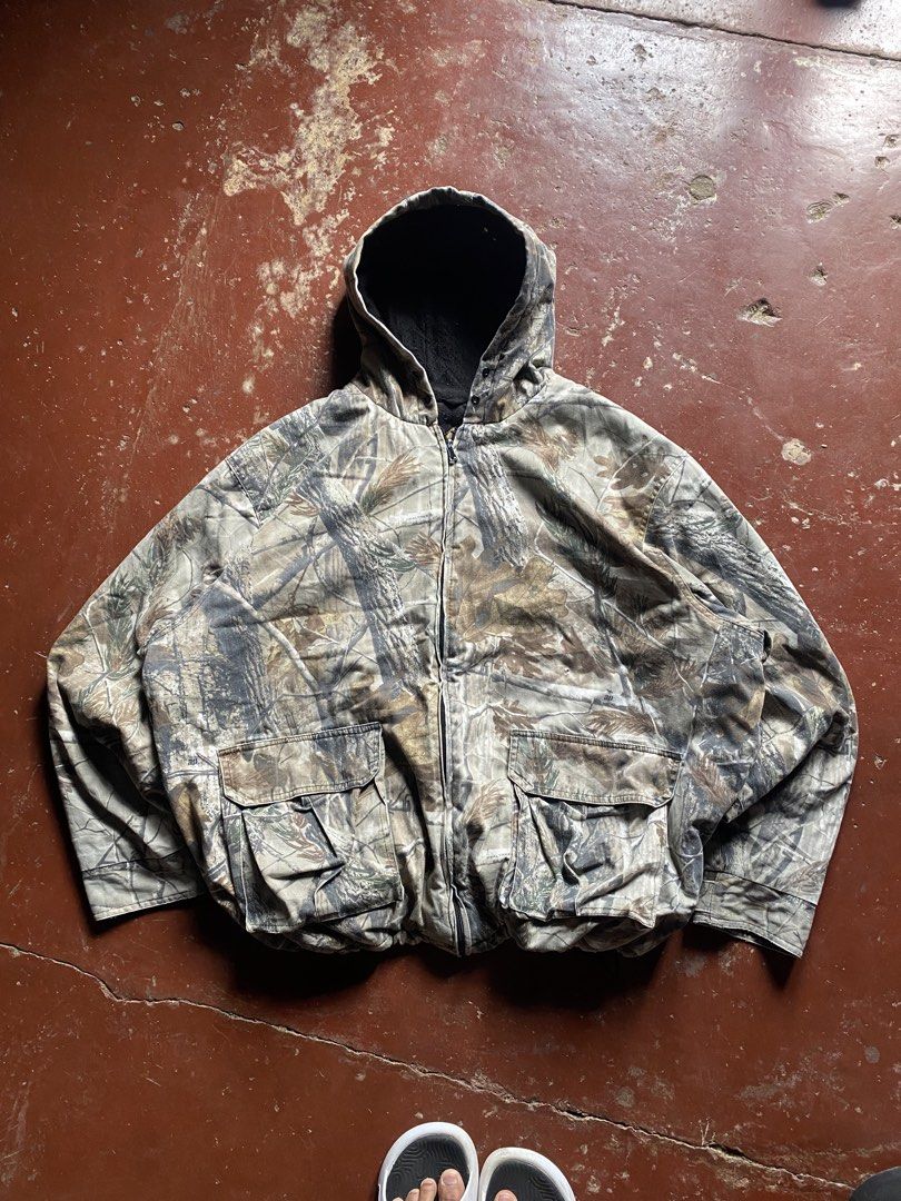 Realtree Camo Zip-Up Hooded Jacket (Category: Coats, Jackets and Outerwear) located in Manila. Submitted by dripxthrift0912 (Listing ID 1464990145, Image 1). Description: - Authentic Realtree tree and leaf camo pattern - Heavy-duty thick canvas exterior for durability - Warm black thermal lining inside - Attached hood for extra weather protection - Two large front cargo pockets with secure flap closures - Ideal for outdoor activities or rugged ca