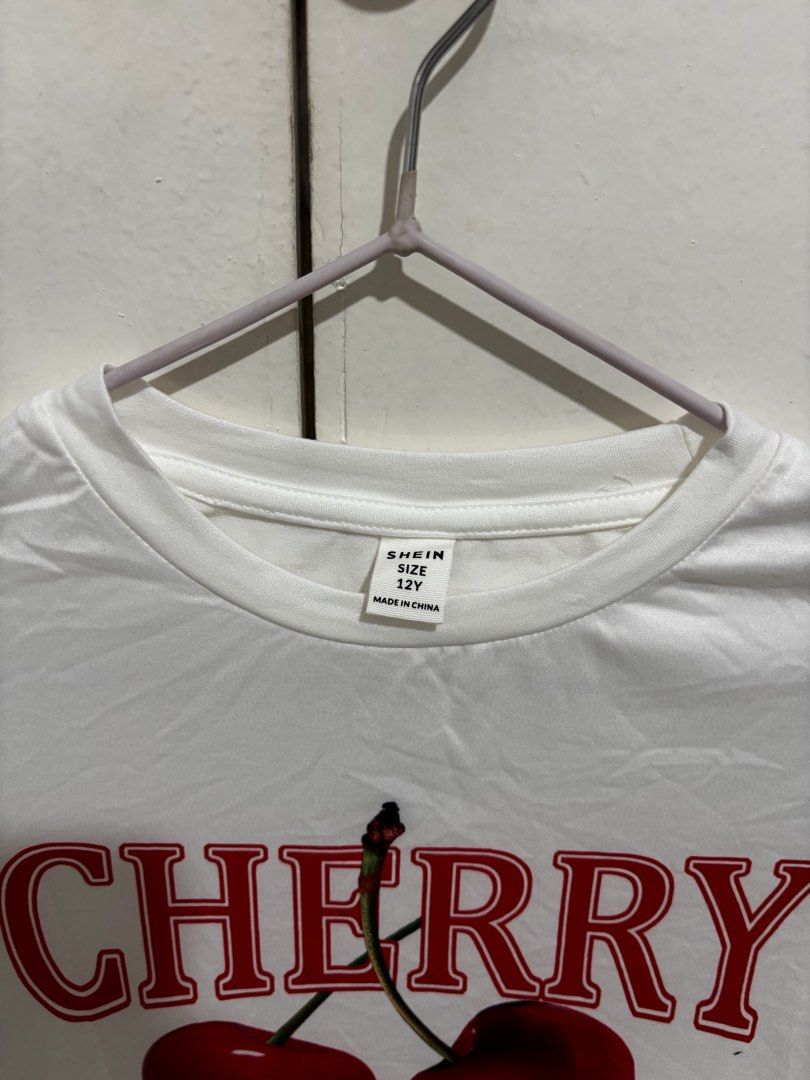 Shein Cherry Graphic White T-shirt (Category: Shirts) located in Manila. Submitted by dianafayesimbre (Listing ID 1465072291, Image 3). Description: White short-sleeve tee from Shein. Red cherry graphic print on the front with text lettering. Round neckline. Size 12Y tag on tag but can fit xs to semi medium womens. Plain solid white back. Lightweight fabric, easy to style with jeans or skirts..