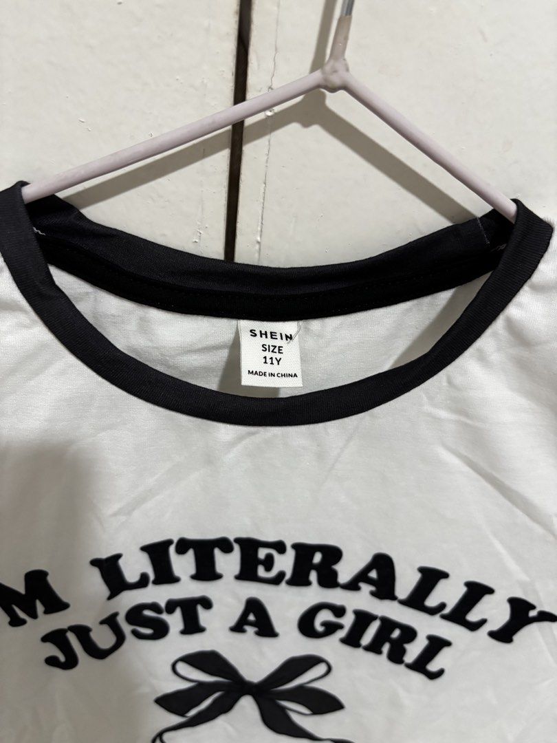 Shein White Ringer Graphic Shirt (Category: Shirts) located in Manila. Submitted by dianafayesimbre (Listing ID 1465072748, Image 2). Description: - Brand: Shein - Size: 11Y on tag but can fit xs to medium - Color: White with black contrast trim on collar and sleeves - Design: Front graphic reads 'I'm literally just a girl' with a black ribbon bow underneath (plain back) - Fabric: Lightweight and comfortable.