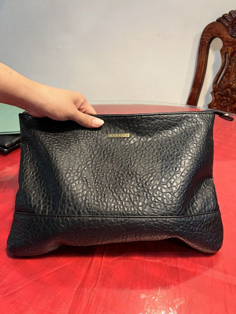 Sisley Black Textured Pouch Clutch (Category: Clutches) located in Manila. Submitted by harpymonetttt (Listing ID 1465104800, Image 3). Description: - Brand: Sisley - Material: Black faux leather with a textured pebble finish - Hardware: Gold-tone Sisley logo plate on front - Closure: Top zipper with dark pull tab - Interior: Fully lined with black fabric, includes one open slip pocket - Condition: Clean interior and exterior, excellent pre-loved