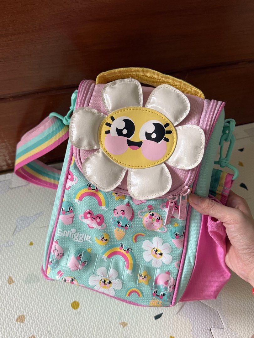 Smiggle Flower Lunch Box Bag with Rainbow Strap (Category: Shoulder Bags) located in Cebu City. Submitted by limjennif52235 (Listing ID 1464979865, Image 1). Description: - Authentic Smiggle insulated lunch bag in a mint green, pink, and yellow colorway - Features fun floral, rainbow, and ice cream graphics with a big smiling flower patch - Keeps food fresh with a silver insulated lining and includes a name tag label under the lid - Offers extra 