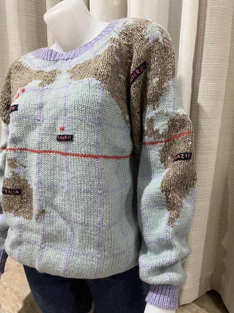 Studio New York World Map Knit Sweater Size M (Category: Longsleeves) located in Tarlac. Submitted by thriftygoodss (Listing ID 1465100895, Image 2). Description: Vintage Studio New York knit sweater. Light blue base with purple grid lines and brown textured continents. Features embroidered location labels like China, Japan, Hawaii, Australia, UK, France, Arabia, and Africa. Ribbed purple collar, cuffs, and hem. Size M tag inside. Made in Hong Ko