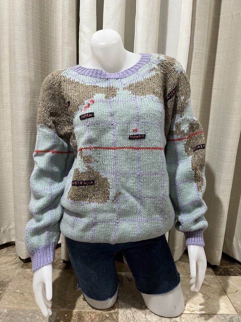 Studio New York World Map Knit Sweater Size M (Category: Longsleeves) located in Tarlac. Submitted by thriftygoodss (Listing ID 1465100895, Image 1). Description: Vintage Studio New York knit sweater. Light blue base with purple grid lines and brown textured continents. Features embroidered location labels like China, Japan, Hawaii, Australia, UK, France, Arabia, and Africa. Ribbed purple collar, cuffs, and hem. Size M tag inside. Made in Hong Ko